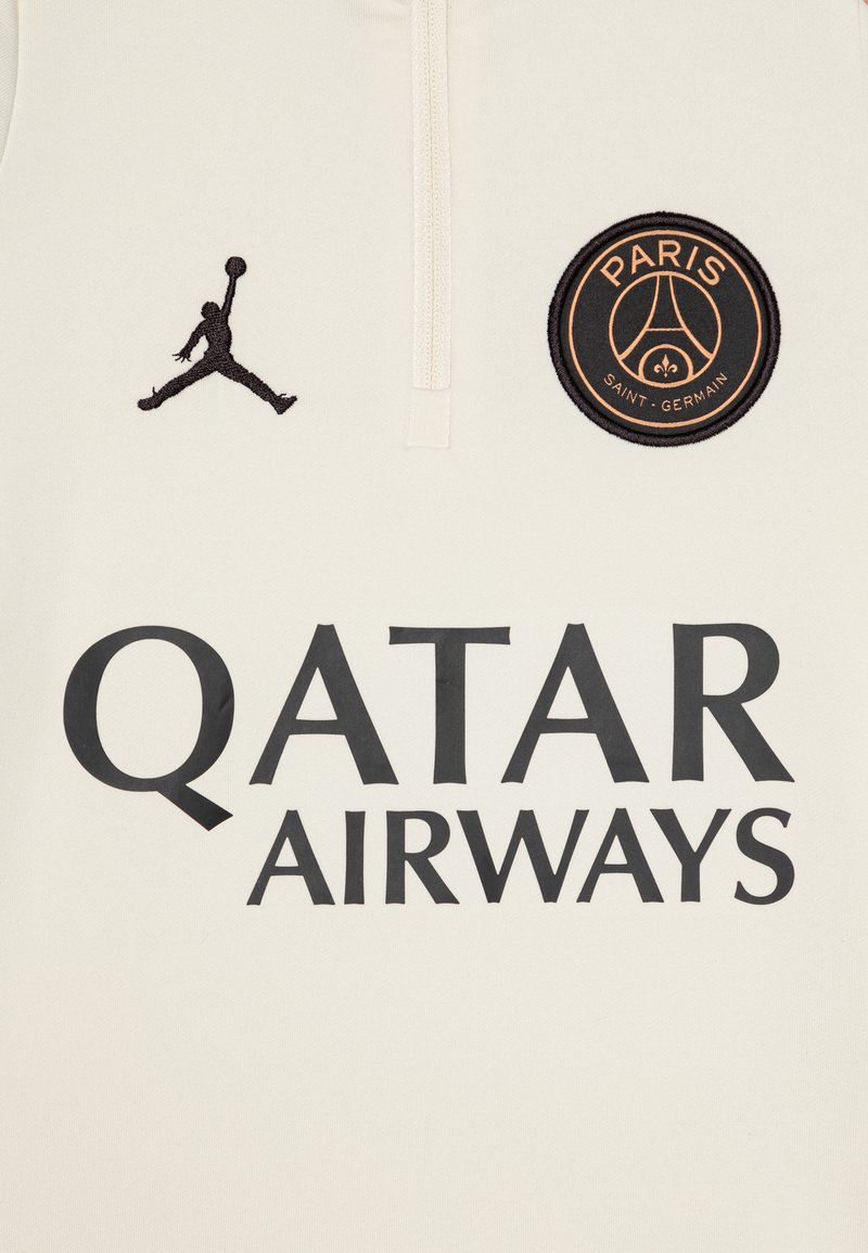 Maillot de sport de couleur crème avec le logo Jordan brodé en noir, un emblème rond du PSG, et un texte en gras noir "QATAR AIRWAYS" sur le devant.