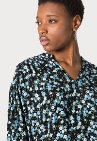 Blusa preta com padrão floral, apresentando pequenas flores azuis e brancas, decote em V e mangas franzidas. Feita de um tecido leve com uma textura suave.