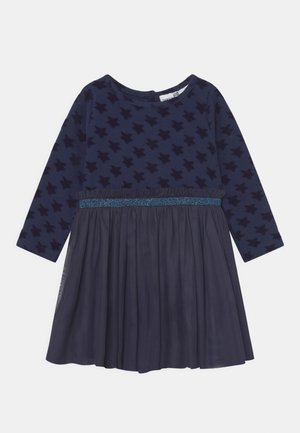 Vestido de manga longa azul-marinho com padrão de estrelas na parte superior, um cós brilhante e uma saia de tule em camadas. Tecido suave com textura lisa.