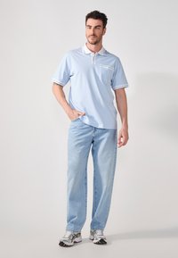 Ljusblå polo med vit krage och fickdetalj, kombinerad med ljus tvättade raka jeans och silvriga träningsskor.