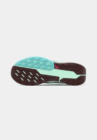 Semelle de chaussure de course avec une bande de roulement en caoutchouc turquoise et marron, des motifs de grip rectangulaires et un petit logo rose près de la zone de la voûte plantaire.