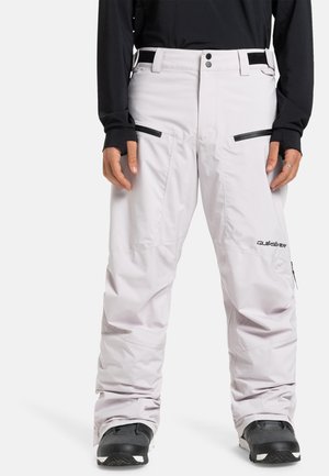 Pantalons de neige rose clair avec une coupe décontractée, poches zippées, passants de ceinture et accents noirs. Le tissu semble lisse et durable.