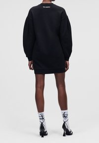 Robe sweat-shirt noire oversize avec manches longues et encolure ronde. Présente un ourlet côtelé, un logo discret à l'arrière, et un matériau texturé.