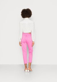 Blusa blanca con lunares negros, pantalones rosa de cintura alta y sandalias blancas. Los pantalones tienen un ajuste slim y una longitud cropped.