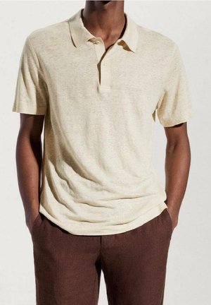 Polo shirt beige clair en tissu doux, avec un col classique, une patte de boutonnage à trois boutons et une coupe décontractée. Associé à un pantalon marron.