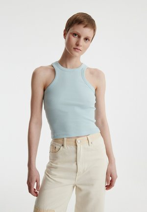 Helles blaues geripptes Crop-Top mit hohem Ausschnitt und ärmellosem Design, kombiniert mit hochgeschnittenen cremefarbenen Hosen mit einer Fronttasche.