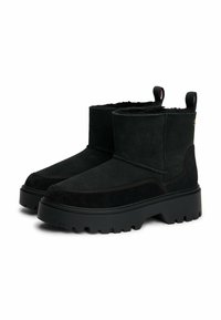 Zwarte enkellaarsjes van suede met een gestructureerde bovenkant, voorzien van een chunky rubberen zool, treklipjes en zichtbare stiksels.