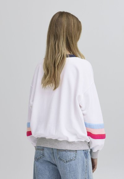 Hvit genser med grå ribbestrikket kant, oversized passform og flerfargede striper i blått, rosa og rødt på ermene.