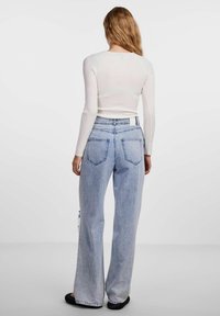 Top a maniche lunghe a coste bianco abbinato a jeans ampi azzurri con due tasche posteriori e un design minimalista.