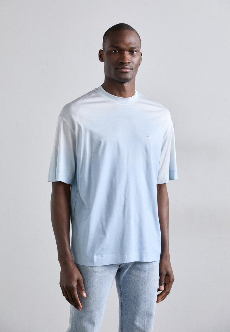 Ανοιχτό μπλε βαμβακερό μπλουζάκι με στρογγυλή λαιμόκοψη και κοντά μανίκια, που διαθέτει ένα μικρό λογότυπο στο στήθος και χαλαρή εφαρμογή. Μπλε τζιν παντελόνι σε casual στυλ.