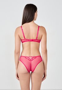 Set di lingerie rosa trasparente con bordo in pizzo sui pantaloni e spalline regolabili sul reggiseno, che mette in risalto una texture liscia e un design aderente.