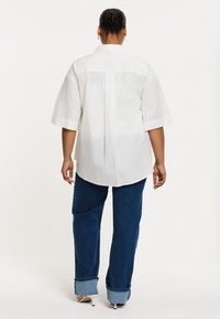 Witte, oversized button-up shirt met korte mouwen. Gecombineerd met donkerblauwe wijde jeans met opgerolde mouwen. Eenvoudige textuur, minimalistisch ontwerp.