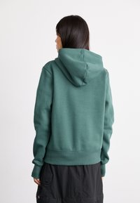 Groene hoodie met een gestructureerde afwerking, geribde manchetten en zoom. Beschikt over een standaard pasvorm en een kangoeroezak.