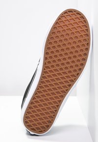 Sole di sneaker nera con motivo di battistrada geometrico, bordatura bianca e gomma marrone testurizzata. Design leggero per presa e durabilità.