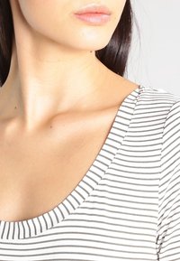 Top z dekoltem w serek wykonany z lekkiego materiału, w czarno-białe poziome paski i o miękkiej fakturze.