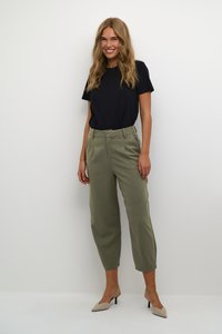 T-shirt noir, pantalon olive ajusté et chaussures à talons beiges. Textures de tissu lisses et coupe structurée.