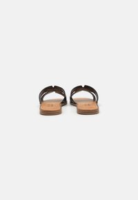 Sandales noires au design minimaliste, avec des découpes et une semelle marron. Fabriquées en matériau lisse avec une forme plate.
