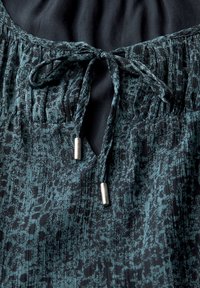 Teal and black patterned fabric top with gathered neckline, featuring a tied drawstring and silver metal accents at the ends.