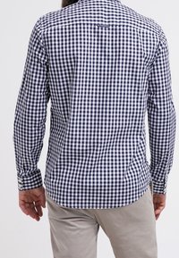 Camicia a quadri bianco e blu navy con maniche lunghe, polsini a bottone e orlo curvo; presenta una spalla a pezzo e dettagli di cucitura visibili.