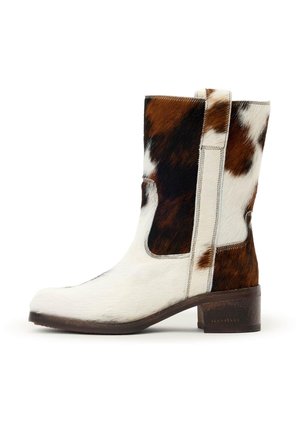 Knöchelhoher Stiefel aus Kuhfell mit braunen, schwarzen und weißen Flecken, einem niedrigen Blockabsatz und einem seitlichen Einziehriemen.