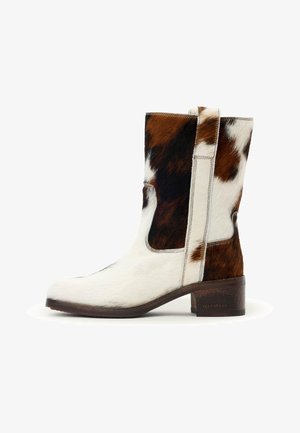 Bota hasta media pantorrilla de cuero de vaca con parches marrones, negros y blancos, tacón bajo de bloque y una tira para ponerla que se tira del lado.