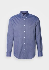 Camicia blu con bottoni realizzata in tessuto misto cotone, caratterizzata da maniche lunghe, colletto classico e un piccolo logo ricamato sul petto.