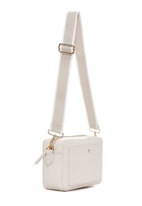 Bolso bandolera rectangular pequeño de color crema con bolsillo delantero, herrajes dorados, cierre superior con cremallera y correa ancha de tela ajustable.