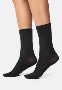 Sorte sokker lavet af glat materiale med en medium riflet manchet. De har et klassisk design og en sømløs tådel for komfort.