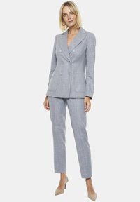 Jasnoszara, dwurzędowa marynarka w fakturowanym materiale z klapami, dwiema przednimi kieszeniami i spodniami o slim fit. Zawiera neutralne beżowe szpilki.