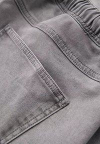 Tejido gris con una textura suave que presenta un bolsillo trasero y detalles de costura sutiles, mostrando un diseño casual y relajado.