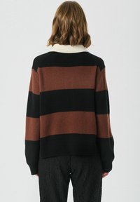 Strikket sweater med brede sorte og brune striber, har en cremet ribbet krave og lange ærmer, lavet af blødt strikkemateriale.