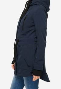 Mörkblå softshell-jacka med huva, dragkedjeförsedd bröstficka, justerbar dragsko i midjan och svarta kantärmar.