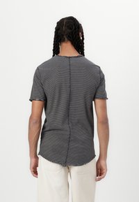 Black and white striped short-sleeve t-shirt with a round neckline and a curved hem. Back seam detail visible. Worn with cream-colored pants.