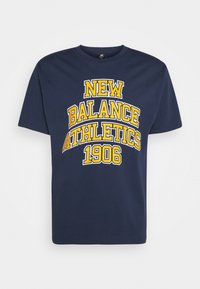 Námořnická modrá bavlněná tričko s výrazným žlutým textem: "NEW BALANCE ATHLETICS 1906" v obloukovém designu. Kulatý límec a krátké rukávy.