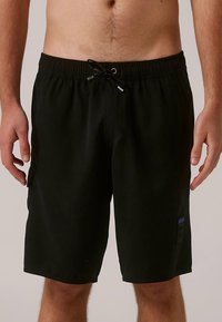 Black swim shorts made of lightweight fabric with an elastic waistband and drawstring. Features a small blue logo patch on the side.