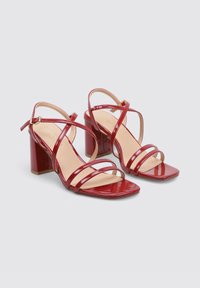 Sandalias de tacón de charol rojo con puntera cuadrada, que presentan múltiples tiras delgadas entrecruzadas y un tacón ancho.