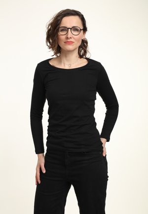 Zwarte langmouwtop met een ronde hals, aansluitend ontwerp en zachte textuur, gecombineerd met zwarte broek. Minimalistische stijl, geen zichtbare patronen.