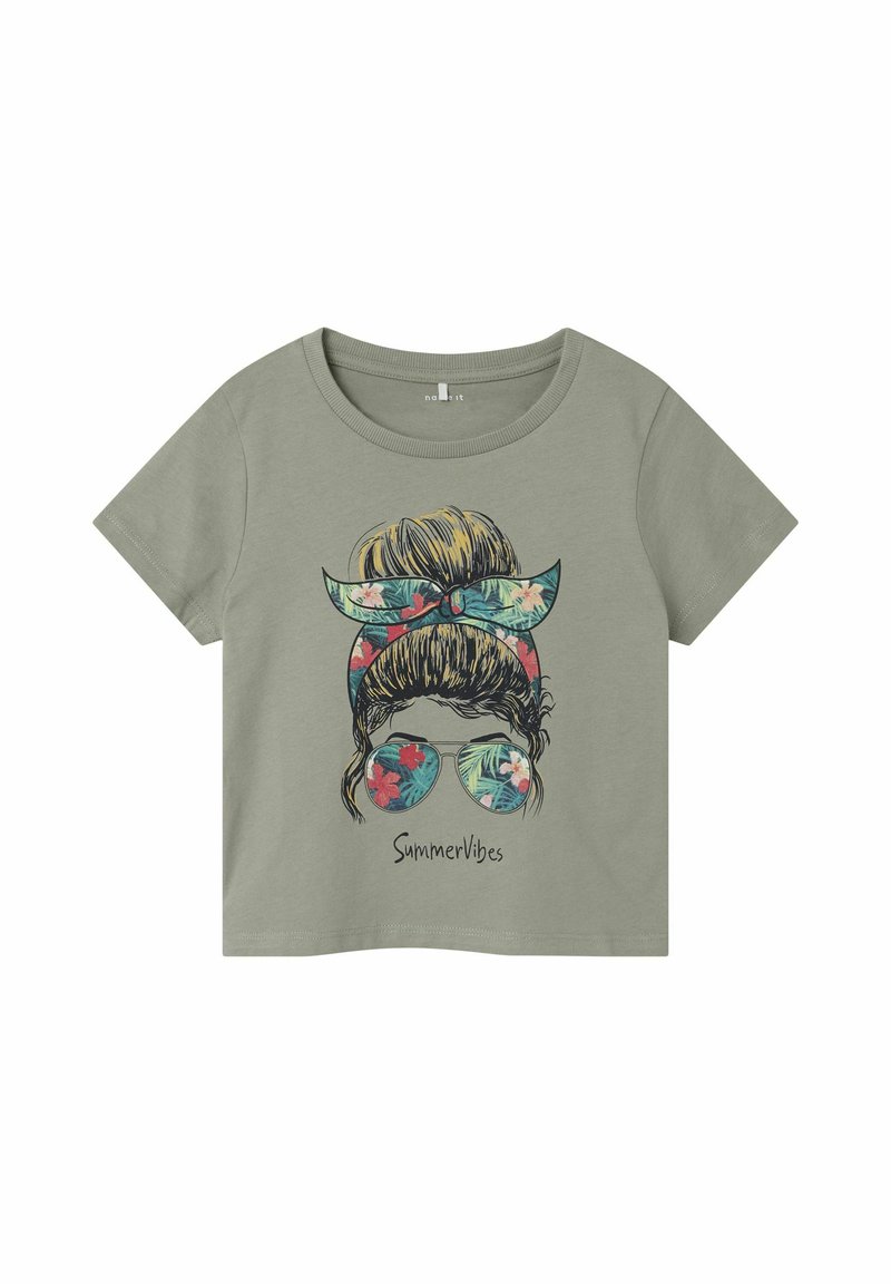 Camiseta corta de algodón verde con gráficos de una persona con una diadema floral y gafas de sol, el texto abajo dice "Vibra de Verano."