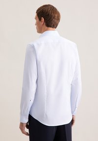 Camicia a maniche lunghe azzurro chiaro con colletto classico, texture liscia, orlo curvo e dettagli con bottoni sui polsini.