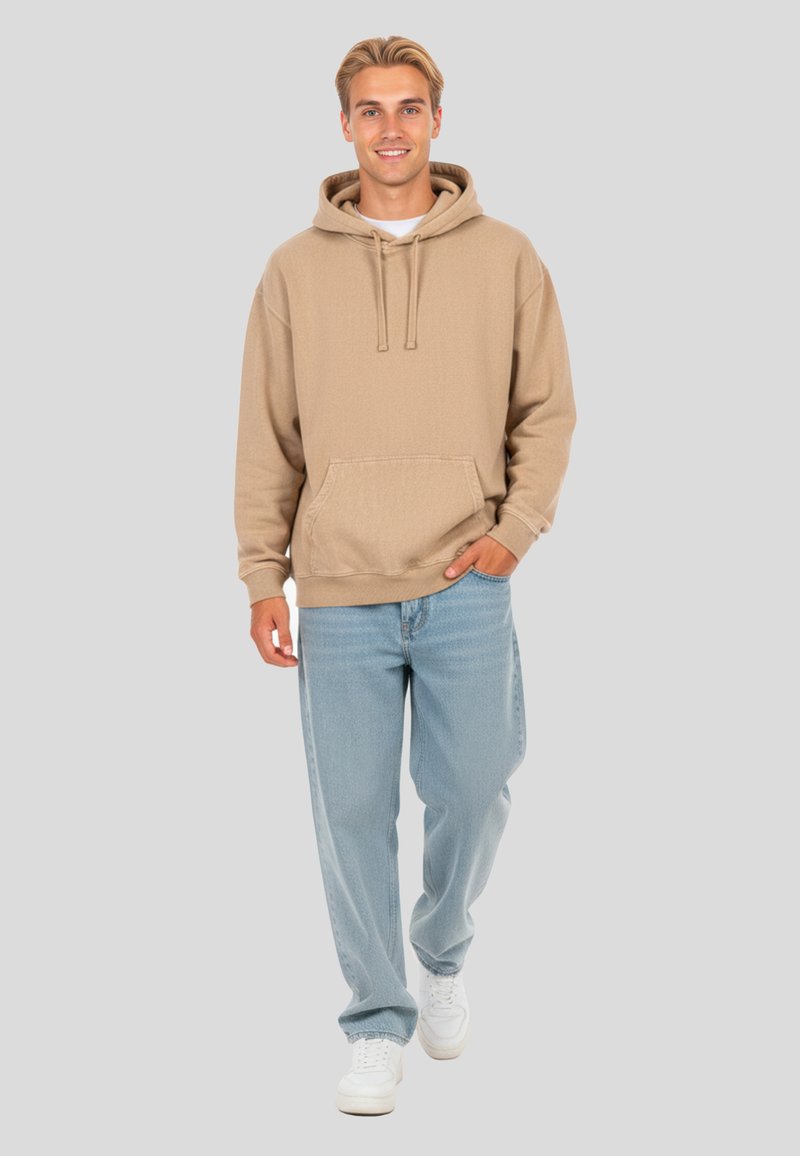 Felpa beige con tasca frontale, cappuccio con cordino e polsini a coste, abbinata a jeans baggy blu chiaro e sneakers bianche.