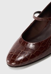 Brown leather Mary Jane shoe with crocodile texture and a thin strap over the instep on a white background.