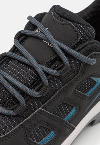 Svart idrottssko med överdel i mesh och grå och turkosa detaljer, runda snören och en texturerad gummisula.