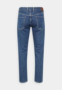 Jeans de denim azul com corte reto, design de cinco bolsos e uma etiqueta de pele castanha na cintura. O tecido tem um acabamento texturizado.