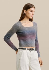 Grauer und lila Farbverlauf Pullover, verkürztes Design, gerippte Textur, quadratischer Ausschnitt, kombiniert mit weißen Hosen und einem schwarzen Gürtel mit einer silbernen Schnalle.