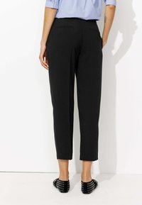 Pantalons noirs, coupés, avec une texture lisse, présentant des poches arrière. Associés à des chaussures plates noires, mettant en avant un design simple.