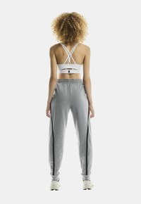 Sutien sport alb cu bretele încrucișate și detaliu tăiat; pantaloni de trening gri cu dungi negre pe laterale; ambele din țesătură ușoară; croială casual.