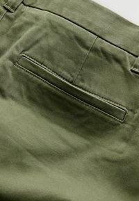 Olive green fabric with a smooth texture featuring a single back pocket. The pocket has a rectangular opening and is stitched along the edges.