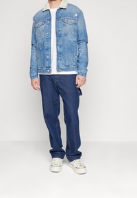 Jeansjacka med ljusblå tvätt, foder av fårull i kragen och slitna detaljer. Kombinerad med mörkblå jeans och vita sneakers.