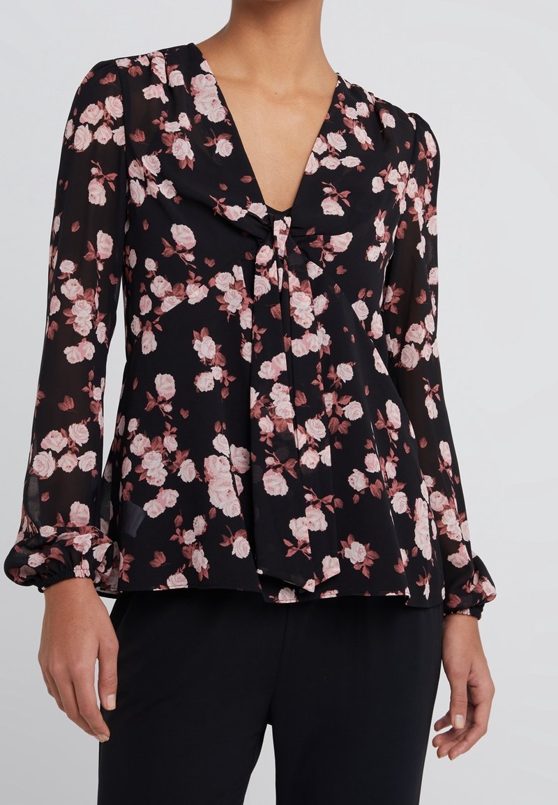 Blusa negra con flores, de mangas largas, escote en V y detalle de lazo en el frente. Presenta un patrón de rosas en tonos rosa y blanco. Tela ligera y transparente.
