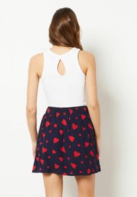 Vitt linne med en nyckelhålsöppning på baksidan, i kombination med en marinblå kjol med spridda röda hjärt-mönster. Bekväm passform och avslappnad design.